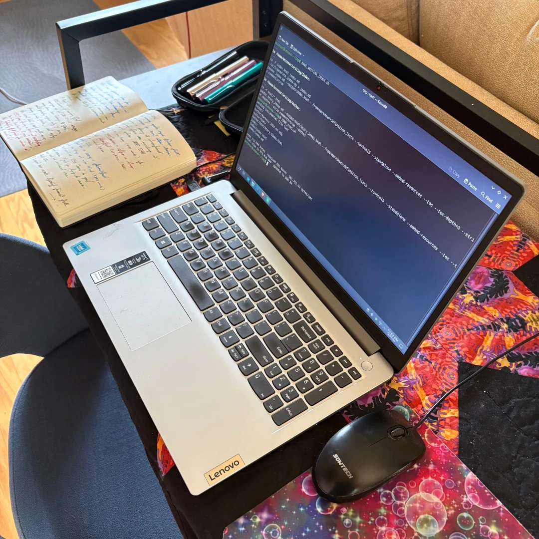 Where I work. Lenovo laptop with Fedora 44. Quilt by my wife Hannah. Leuchtturm1914 notebook and LAMY Al-star fountain pens.
